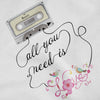 An extreme close-up of a graphic print on white fabric, featuring an illustration of a vintage cassette tape labeled 'THE BEATLES' connected by a winding black line to the cursive phrase 'All you need is' and a decorative pink 'Love' design adorned with two small birds and floral flourishes.