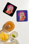 Product lifestyle photograph of two art coasters featuring the BILLU BRBR portrait by Nemozine, displayed on a white surface alongside a glass bowl of pineapple, a jar of honey with a wooden dipper, and a glass of refreshing drink.