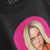 A close-up, angled product shot of a black t-shirt showcasing the detailed print of a stylized portrait of a blonde woman framed by a vibrant pink circle, with a partial view of the collar and brand tag at the top.