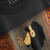 An angled, close-up product shot of a black t-shirt showing a detail of the graphic print, which features a stylized lion wearing headphones with smoke swirling from its mouth, set against a textured, vintage-style background, with the brand tag visible near the collar.