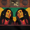 An extreme close-up of a graphic print on dark fabric, showcasing a mirrored pop-art style portrait of Bob Marley smiling. The illustration is set against a textured background of red, gold, and green, with a partial view of the text 'Iron like Lion in Zion' visible along the top edge.