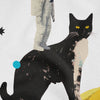 An extreme close-up of a graphic print on white fabric featuring an astronaut figure standing on the back of a large black-and-white cat, with a small blue circle and a black star shape in the background, all set against a white t-shirt texture.
