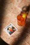 Product lifestyle photograph of an art coaster featuring the FLOWERY portrait design featuring Van Gogh in foliage, by Nemozine, displayed on a polished marble surface next to a cocktail garnished with a lemon twist.