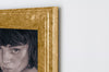 closeup of a golden wooden frame on a white wall, with a charcoal portrait of a woman with beautifully rendered features