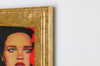 A beautiful acrylic painting of a woman's face with a luxurious rich gold frame on a white wall