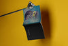 Product lifestyle photograph of an art cover sketchbook featuring a stylized, colorful owl design by Nemozine, suspended against a vibrant yellow background.