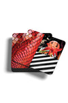 Product photograph of a neat stack of square coasters, with the top coaster angled to display a graphic design featuring red tiled patterns, black and white horizontal stripes, and stylized cartoon characters, isolated against a clean white background.