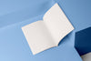 An open, blank sketchbook with white pages, positioned against a blue geometric background.