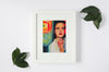 Lifestyle product photograph of the limited edition archival art print SMOKD OYSTR by Nemozine, displayed in a white frame on a clean surface, accented with scattered green leaves.