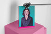 Product lifestyle photograph of an art cover sketchbook featuring the ZAHIR portrait by Nemozine, suspended above a vibrant pink platform against a clean white background.